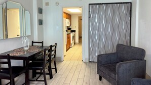 Uma área de refeições com mesa e cadeiras, um sofá, cozinha ao fundo e uma porta deslizante estampada.