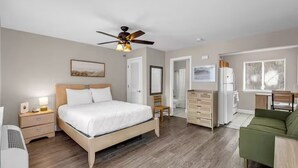 Une chambre à coucher comprenant un lit, des tables de chevet, une commode, un ventilateur de plafond et une fenêtre.