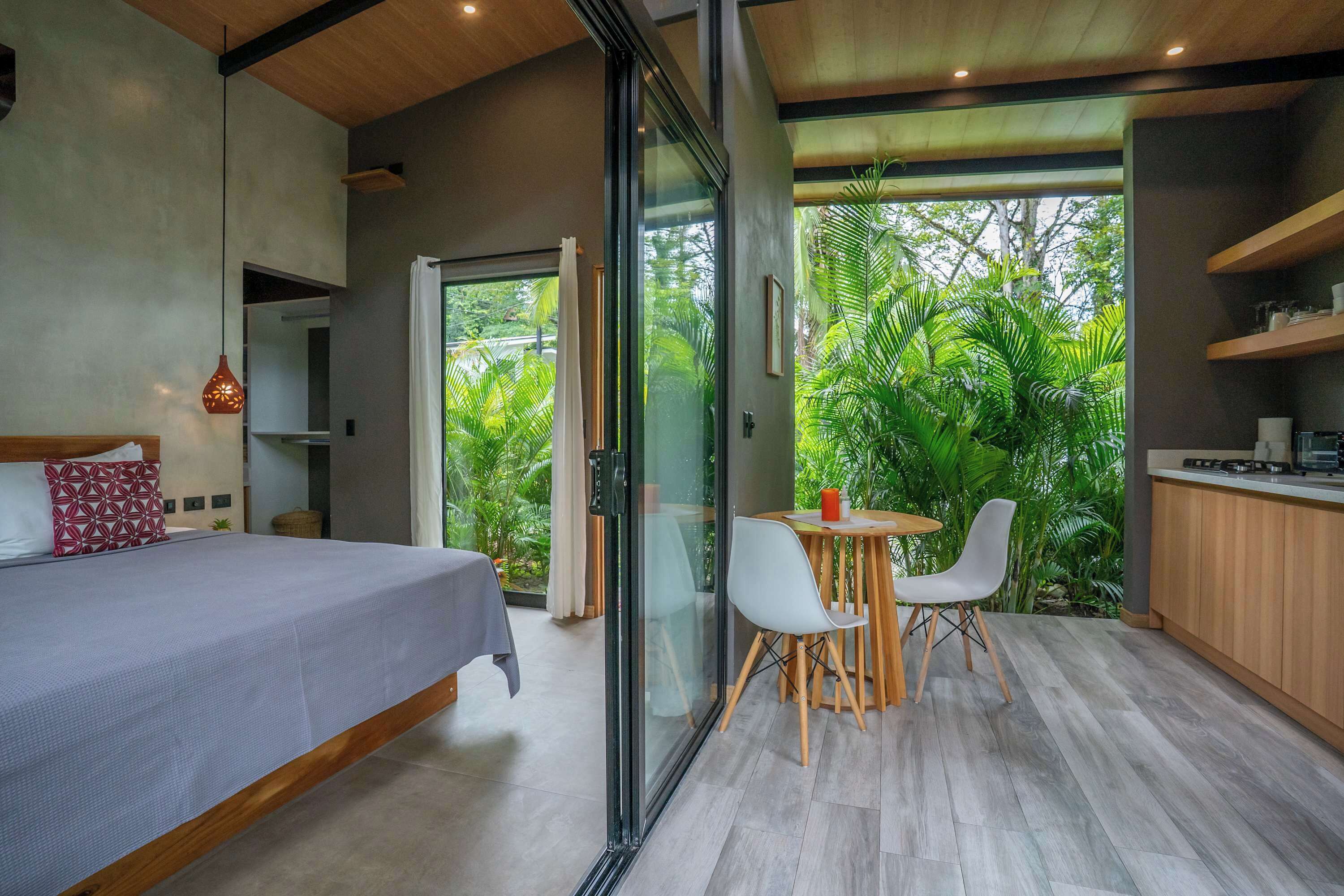 A modern bedroom with a bed, a glass door leading to a balcony with a dining area and kitchen.