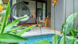 Ein modernes Interieur mit Hängekorbschaukel, kleinem Tisch und Poolanlage, umgeben von Grünpflanzen.