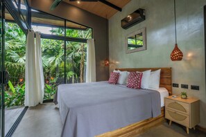 A bedroom with a large bed, a nightstand, a mirror, and a view of greenery outside. - Raya Bungalow, AC & Plunge Pool (Punta Uva)