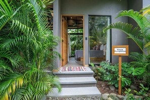 A modern bungalow with a wooden door, a small outdoor seating area, and lush tropical plants. - Raya Bungalow, AC & Plunge Pool (Punta Uva)