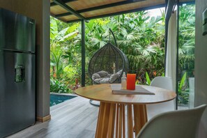 A modern kitchen with a built-in refrigerator, a dining area with a round wooden table, and a hanging chair. - Raya Bungalow, AC & Plunge Pool (Punta Uva)