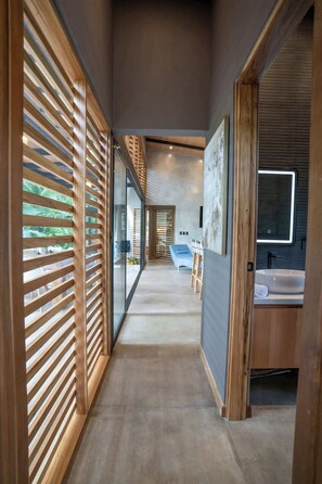 Un couloir moderne avec des lambris en bois, un canapé bleu et une salle de bain équipée d’un lavabo et d’un miroir.