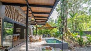A modern outdoor pool area with a wooden pergola, lounge chairs, and a glass-enclosed dining area. - Villa Asencia w/ pool & AC near the beach (Punta Uva)