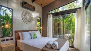 A bedroom with a large bed, a nightstand, a wall-mounted air conditioner, and a view of greenery through the window. - Villa Asencia w/ pool & AC near the beach (Punta Uva)