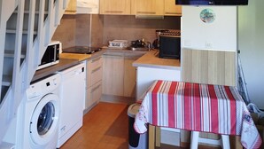A compact kitchen with a washing machine, a dining table with a striped tablecloth, and a TV mounted on the wall. - Apartment (Argelès-sur-Mer)