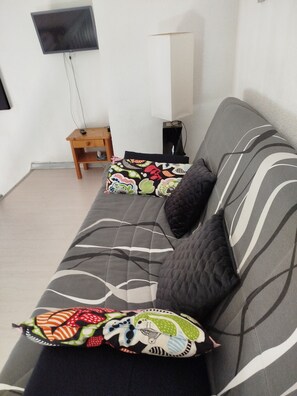 A living room with a sofa, pillows, a small wooden table, and a television mounted on the wall. - Apartment (Argelès-sur-Mer)
