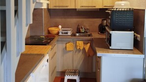 A compact kitchen with wooden cabinets, a microwave, a coffee maker, and a small stool. - Apartment (Argelès-sur-Mer)