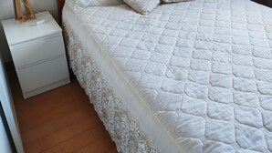 A neatly made bed with a wooden headboard, a white nightstand with a lamp, and a patterned pillow. - Apartment (Argelès-sur-Mer)