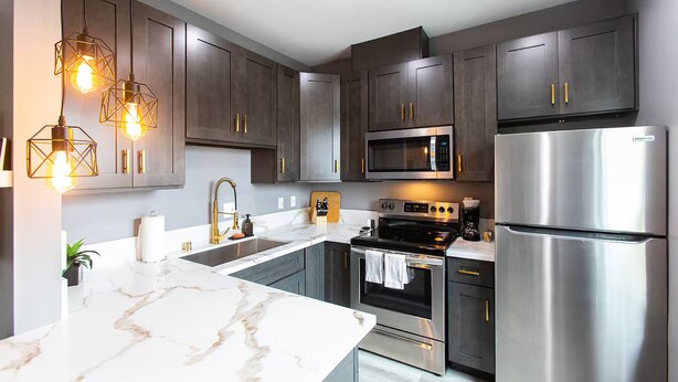 A modern kitchen with dark cabinets, stainless steel appliances, and a marble countertop.