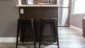 Two black bar stools with a dark countertop and a stainless steel refrigerator in the background.