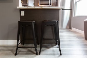 Two black bar stools with a dark countertop and a stainless steel refrigerator in the background. - Stylish King Suite Steps to Dining & Parks (San Diego)