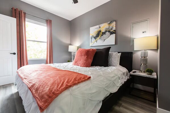 A bedroom with a bed, a nightstand, a lamp, and a window with curtains. - Stylish King Suite Steps to Dining & Parks (San Diego)