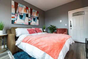 A bedroom with a bed, a chair, a door, and a painting on the wall. - Stylish King Suite Steps to Dining & Parks (San Diego)