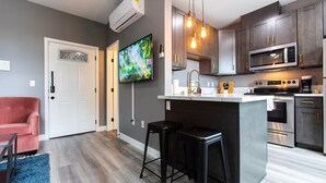 A modern kitchen with a central island, stainless steel appliances, and a flat-screen TV mounted on the wall.