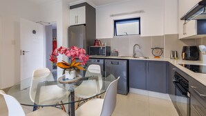 A modern kitchen with grey cabinets, a stainless steel refrigerator, and a glass dining table with chairs. - Haus of Salt (Ballito)