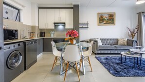 A modern kitchen with a dining area, a gray sofa, and a blue rug. - Haus of Salt (Ballito)