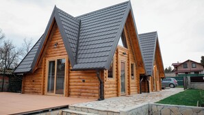 Une cabane en rondins avec un toit en pente, des marches en pierre menant à l’entrée et une terrasse dallée.