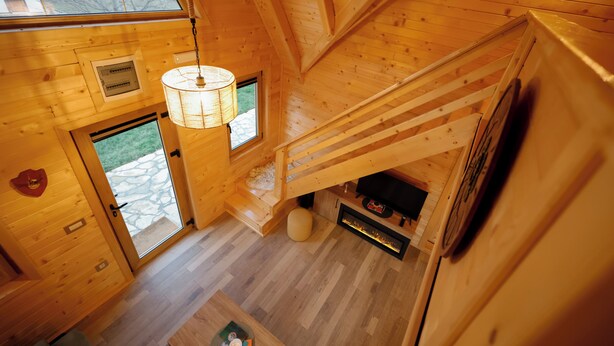 L’intérieur d’un chalet en bois, avec un escalier, une cheminée et une vue sur l’extérieur.