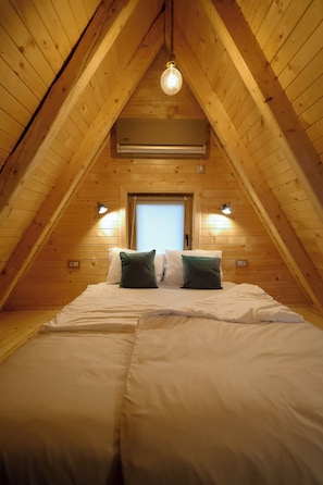 A cozy attic bedroom with a sloped ceiling, a bed with white and green bedding, and two wall-mounted lights.