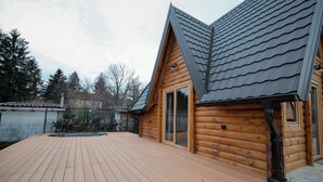 Une cabane en bois dotée d’une terrasse, d’une cheminée et d’une grande fenêtre.