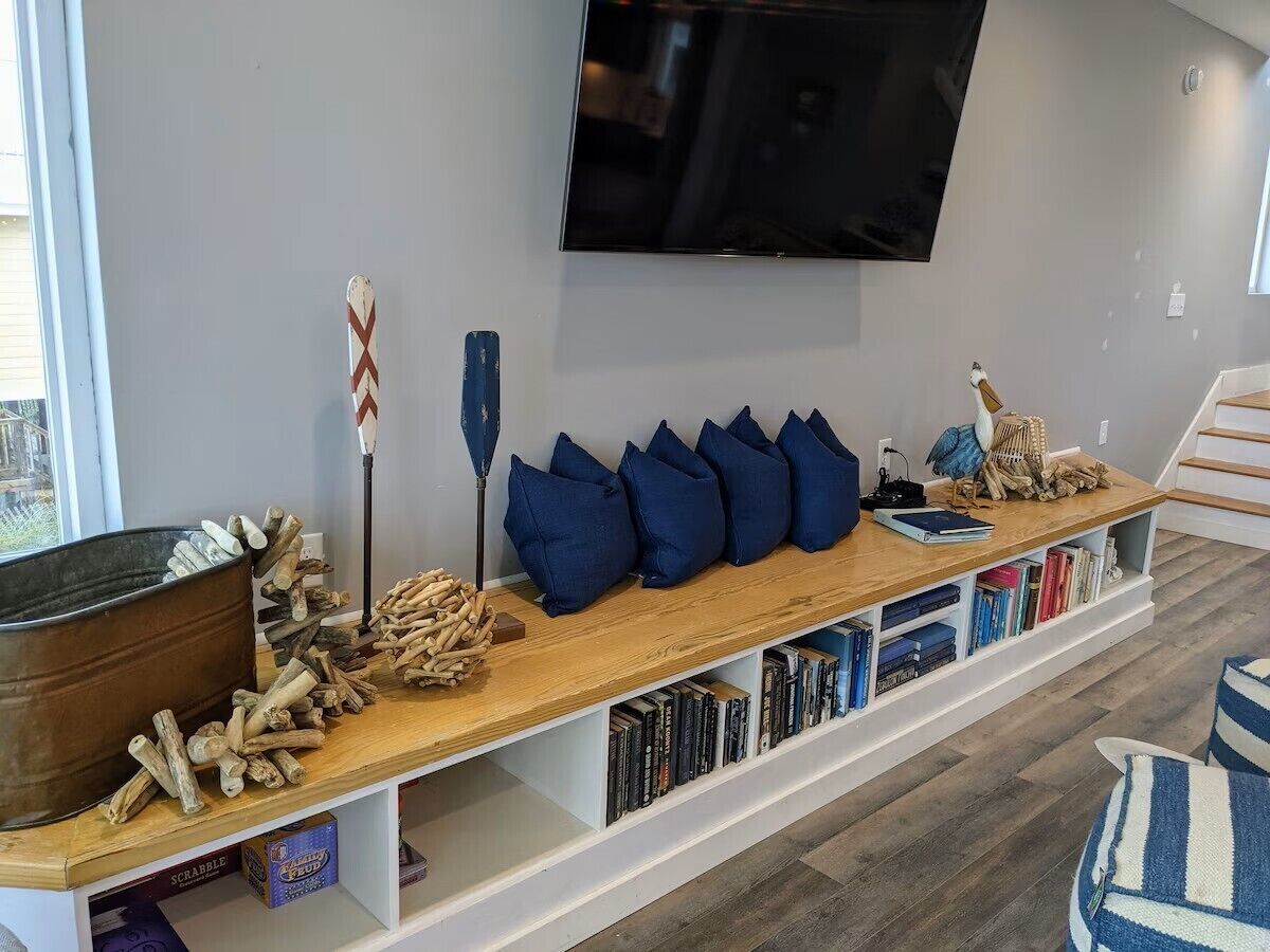 A living room with a long wooden bench, a television mounted on the wall, and a bookshelf filled with books.