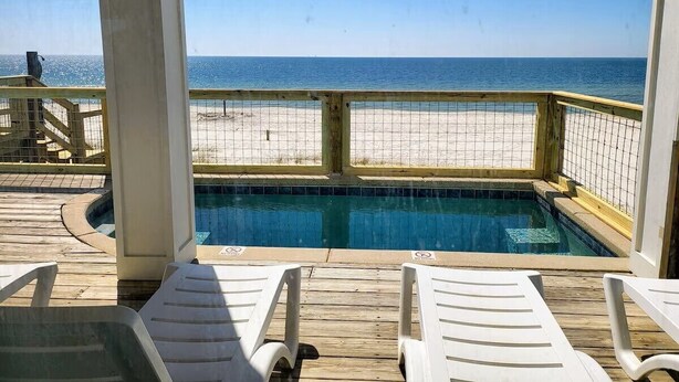 Zwembadgedeelte met een houten terras, witte loungestoelen en uitzicht op strand en zee.