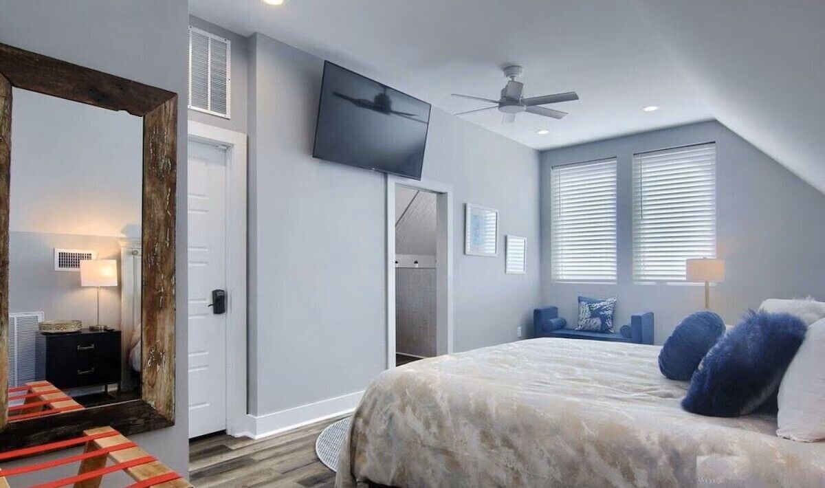 A bedroom with a bed, a TV, a ceiling fan, and a window with blinds.