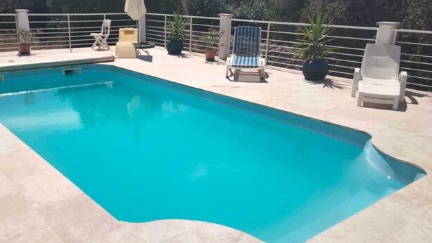 Piscina rectangular con borde de baldosas, rodeada de plantas en macetas y sillas de descanso.