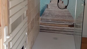 Un baño con una puerta de cristal que da a una vista simulada del océano, una zona de ducha y un perchero blanco.