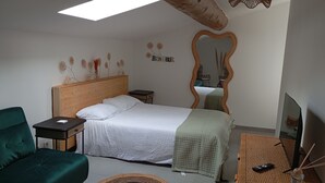 Un dormitorio con una cama, un sillón verde, una mesita de noche, un espejo y un televisor.
