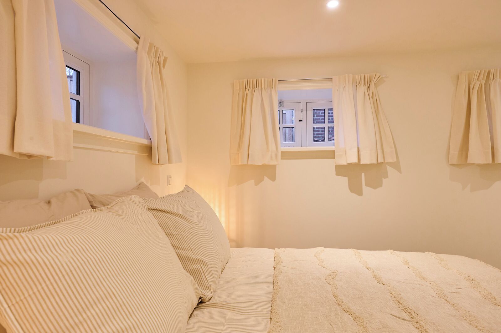 A bedroom with a large bed, two windows with curtains, and a view of the outside.