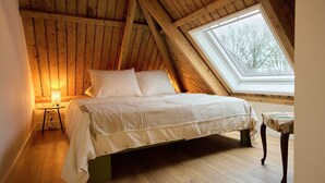 A bedroom with a sloped ceiling, a bed, a bedside table with a lamp, and a window. - Cottage 58B (Twisk)