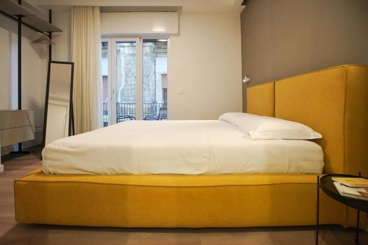 A hotel room with a bed, a small table, and a view of the outside balcony.