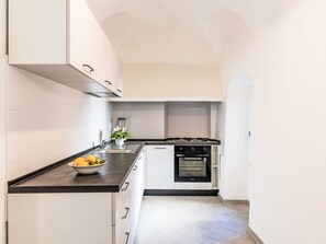 Une cuisine étroite avec des meubles blancs, un plan de travail noir, une cuisinière à gaz et un four.