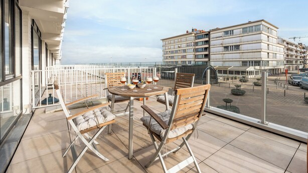 Een balkon met een tafel en stoelen, uitzicht op een gebouw en een heldere lucht.