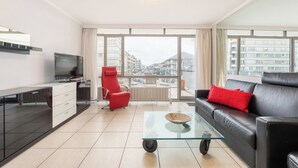 Een moderne woonkamer met een bank, een rode fauteuil, een glazen salontafel en een televisie.