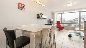 Een moderne keuken met een wit aanrecht, een zwarte stoel en een rode stoel. Er is een raam met uitzicht op gebouwen en een balkon.