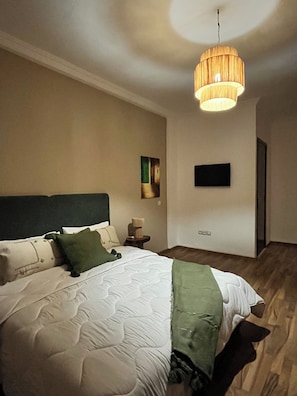 A modern bedroom with a large bed, a bedside table, a wall-mounted TV, and a hanging light fixture. - Superbe appartement au cœur de Marrakech (Marrakech)
