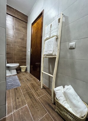 A bathroom with a wooden floor, a white toilet, a wooden door, a towel rack with towels, and a wicker basket. - Superbe appartement au cœur de Marrakech (Marrakech)