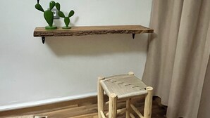 Un petit tabouret en bois, une étagère en bois avec un miroir, et un cactus posé sur l’étagère.