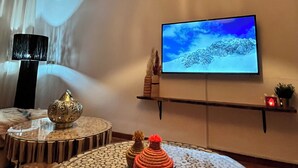 Un salon avec une table ronde, un téléviseur fixé au mur et un luminaire suspendu.