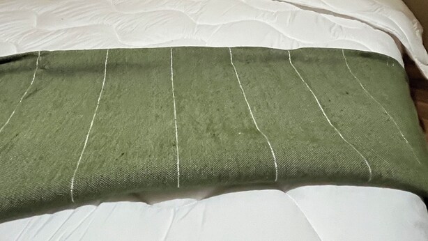 Un lit bien fait, avec une couverture verte, des draps blancs et une tête de lit sombre.