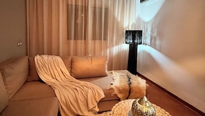 Un salon avec un canapé beige, une table basse ronde agrémentée d’un élément décoratif central, et une grande fenêtre ornée de rideaux légers.