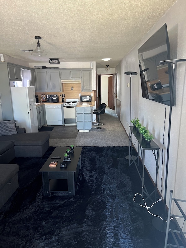 Un espacio habitable compacto con kitchenette, un sofá, una mesa de centro y un televisor montado en la pared.