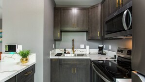 A modern kitchen with dark cabinetry, a stainless steel microwave, and a black stove. - Chic Studio – Steps to Dining, Wi-Fi & A/C (San Diego)