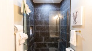A modern bathroom with dark tiles, a glass shower enclosure, and a toilet. - Chic Studio – Steps to Dining, Wi-Fi & A/C (San Diego)