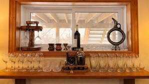 Et vindue med træramme, en flaske vin og forskelligt glas og køkkenudstyr på en træhylde nedenunder.