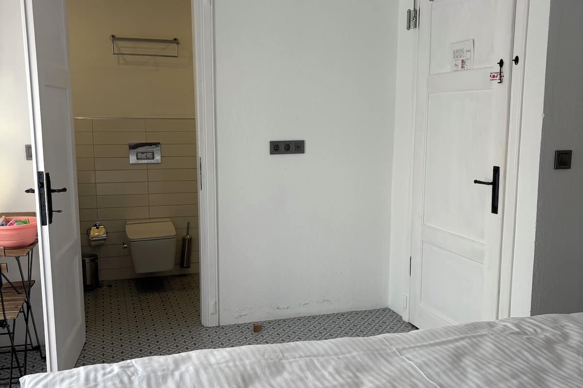 Une chambre à coucher avec un lit, une porte donnant sur la salle de bain et un luminaire suspendu.